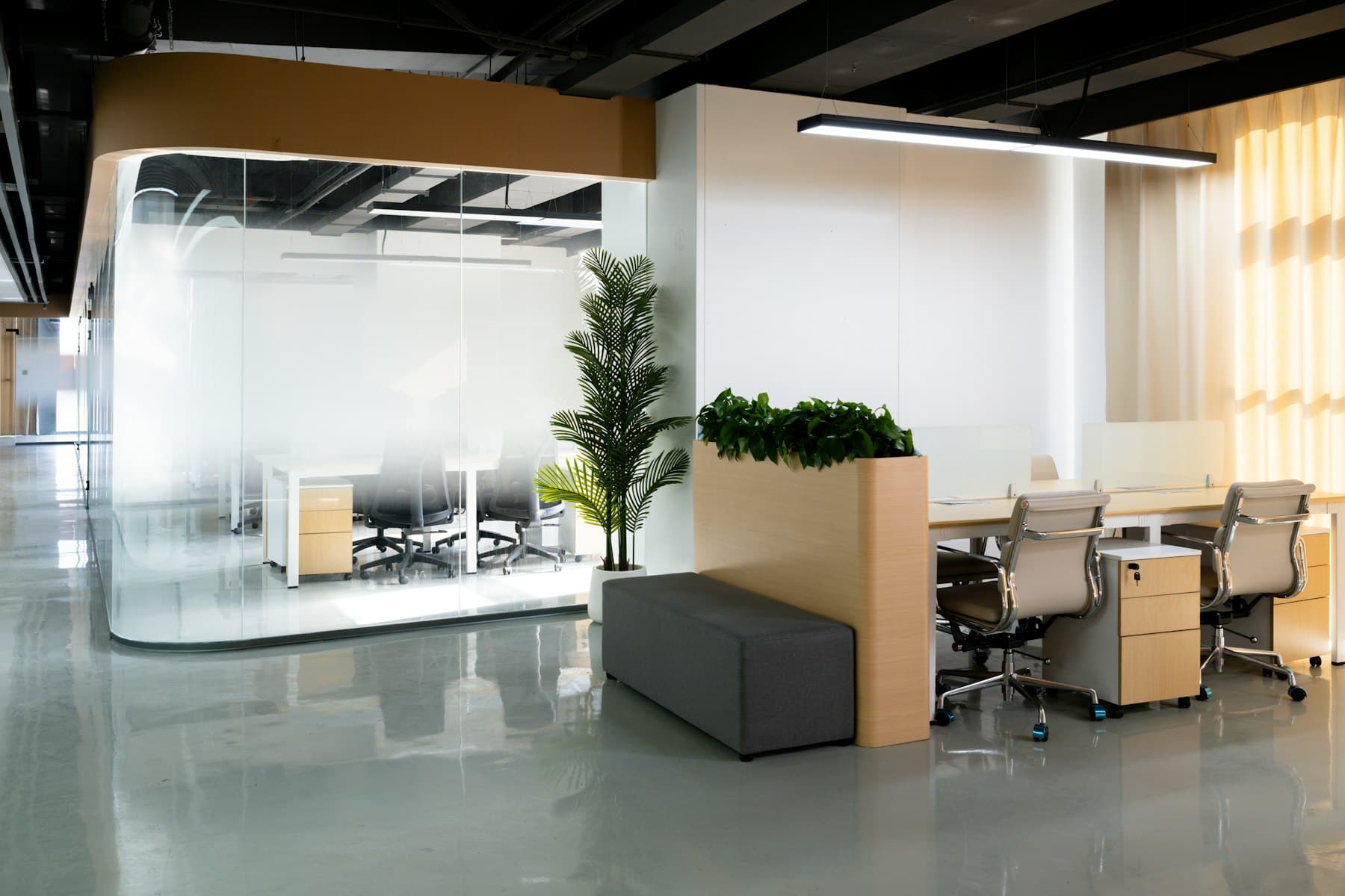 A modern commercial office interior with glass-walled meeting room and workstations