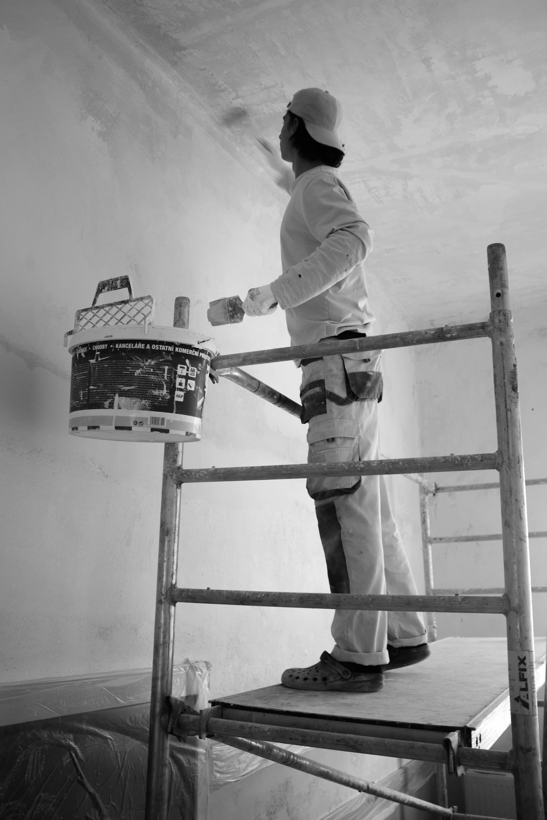 A painter on a scaffold platform cutting in paint along an interior ceiling line